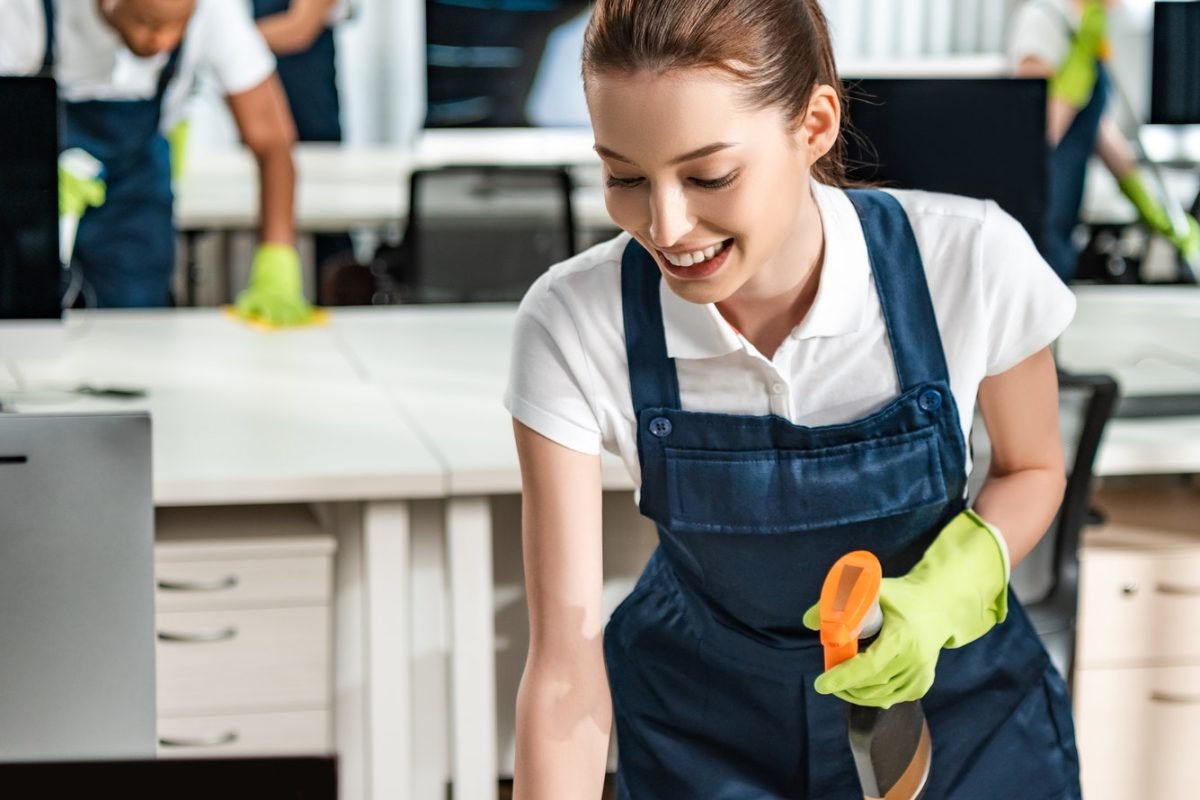 cheerful-cleaner-in-overalls-cleaning-office-desk-with-rag.jpg